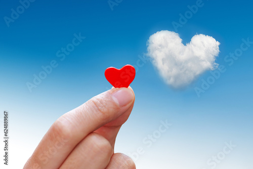 Woman hand holding a red heart against blue sky with heart shape cloud