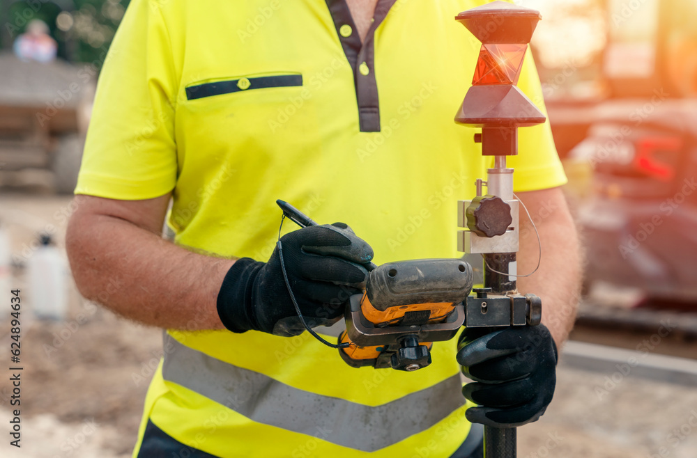 Site engineer surveyor using rugged tablet controller computer to operate EDM total station for setting out and surveying close-up Site engineer surveyor using rugged tablet controller computer to operate EDM total station for setting out and surveying close-up