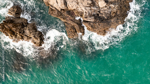 Aerial view directly above waves crashing onto rocky cliffs in Cornwall
