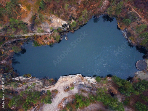 Fototapeta Naklejka Na Ścianę i Meble -  Picturesque aerial view of landscape with emerald lake and rocks in the middle of a coniferous autumn forest in Korostyshiv granite quarry, Zhytomyr district, northern Ukraine. Zhytomyr canyon