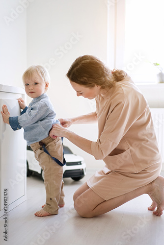 Young mother dressing her child in his pants 