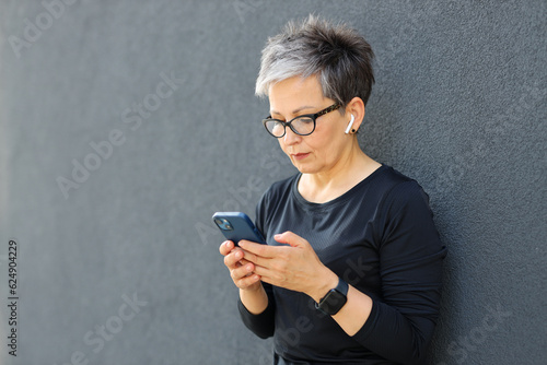 Portrait of a sporty senior woman with headphones and a smartphone in her hands who uses a mobile application.