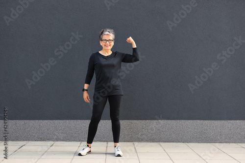 Smiling senior woman in sportswear shows biceps, strength and active lifestyle. © Andrii Zastrozhnov