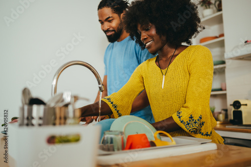 Fotografie A cheerful african american couple is doing dishes and cooking lunch at home together