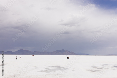A beautiful unusual landscape on which a large desert of white salt and blue mountains in the distance on cloudy day. Bonneville Salt Flats, Utah, USA - 19 June 2023 © Liudmila