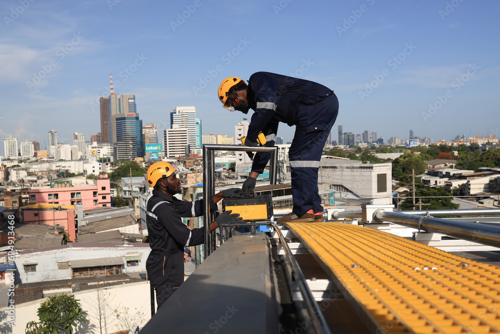 two male mechanical engineers working on the rooftop of a high build ing in the city. checking the condition of the steel pipe on the roof building