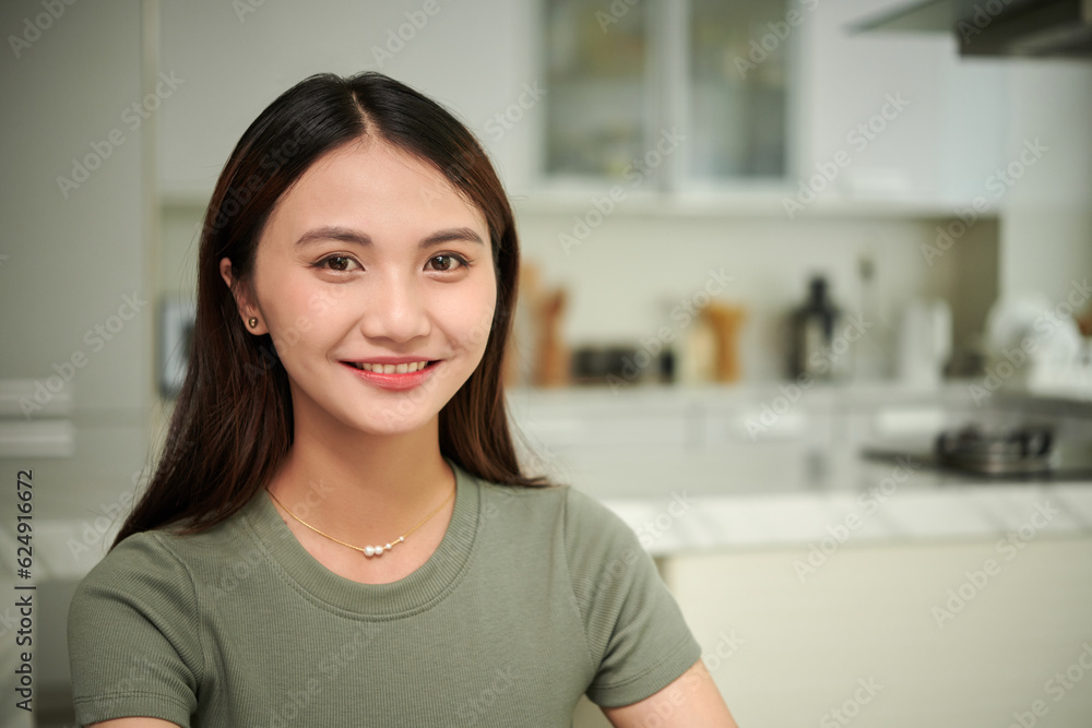 Portrait of cheerful young Asian woman in t-shirt standing in kitchen