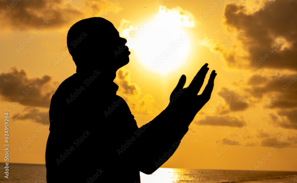 An awe-inspiring photograph capturing the stillness of a lonely man immersed in prayer, his silhouette shining against the backdrop of the fiery solstice sky.