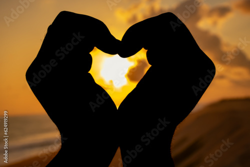 An enchanting picture capturing the silhouette of a hand  fingers arranged in the shape of a heart  illuminated by the warm colors of the setting sun.