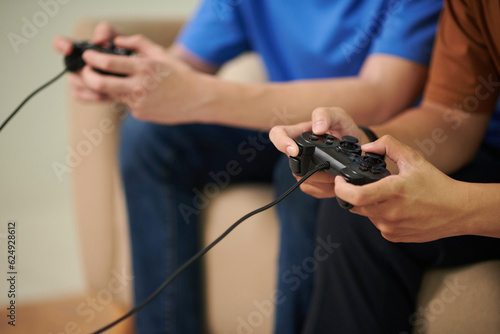 Hands of teenage boys playing videogame together at home