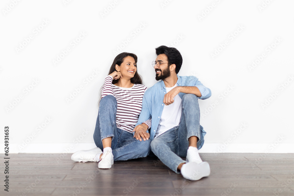 Excited thrilled young indian couple sitting on floor at apartment Excited thrilled young indian couple sitting on floor at apartment