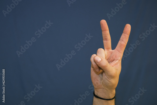 Eine Hand zeigt eine Gebende des Friedens vor blauem Hintergrund