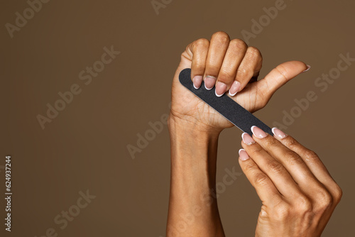 African american middle aged woman with manicure holding nail file isolated on brown background, free space, banner