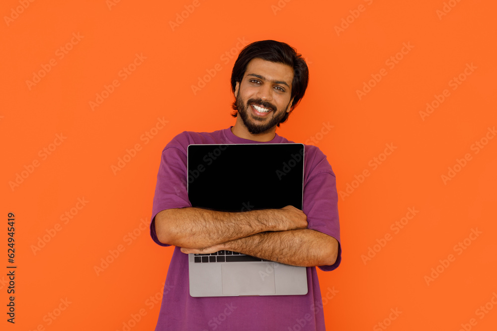 Positive indian man hugging laptop with blank screen on orange Positive indian man hugging laptop with blank screen on orange