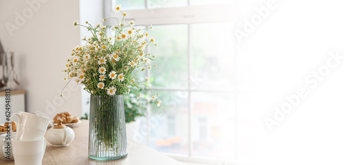 Vase with fresh chamomiles on table in kitchen. Banner for design