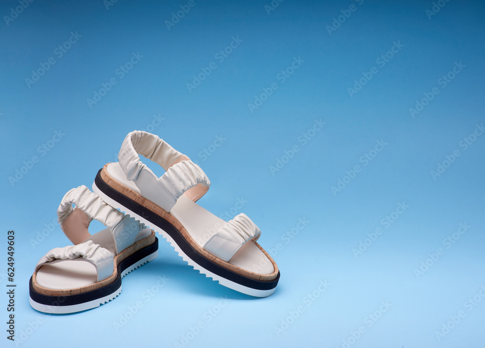 Naklejka premium A shot of new pastel leather sandals with three-colored soles placed one on another. Gradient blue background. Concept of selling shoes