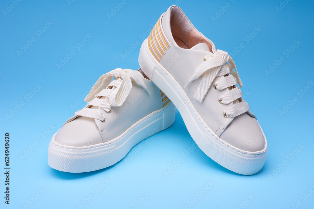 Close up view of trendy modern everyday sneakers on the blue background. Beige leather, pastel and yellow details on the back. Urban style shoes concept.