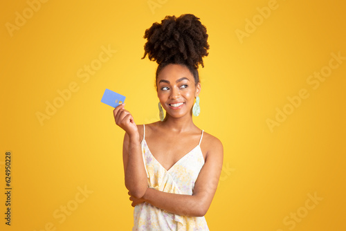Fototapeta Cheerful pensive young black woman show credit card, dreaming about buying