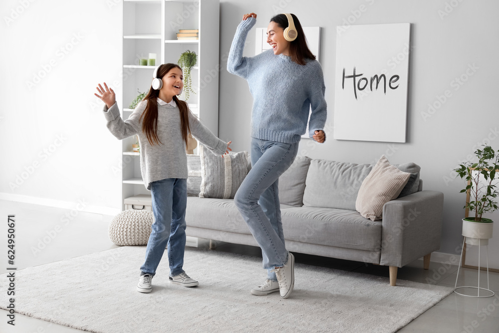 Φωτογραφία Little girl and her mother in sweaters and headphones dancing at home