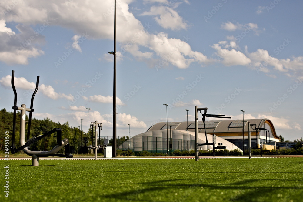 Obraz premium Przyrządy siłowni zewnętrznej na tle innych obiektów sportowych i boisk w słoneczny dzień