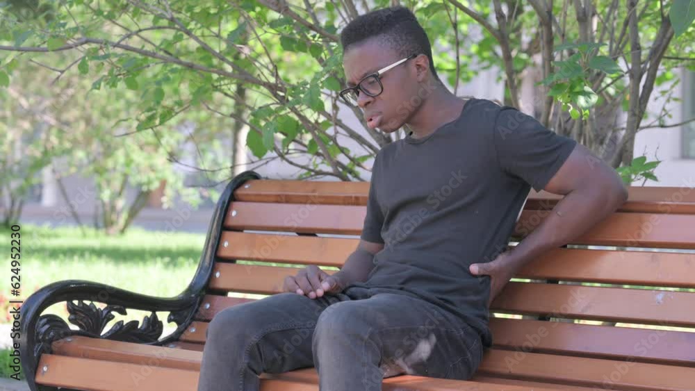 Young African Man Sitting Outdoor with Back Pain Young African Man Sitting Outdoor with Back Pain