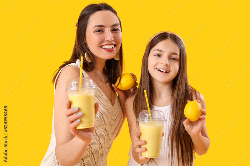 Little girl with her mother drinking lemon smoothie on yellow background Little girl with her mother drinking lemon smoothie on yellow background