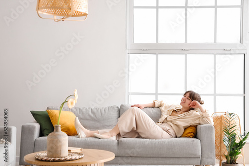Foto Happy young woman lying on grey sofa in interior of light living room