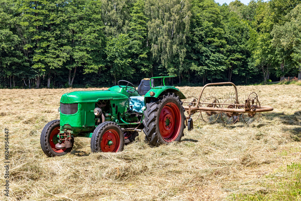 Old farm tractor turning over mowed grass in a meadow. Spring season. Old farm tractor turning over mowed grass in a meadow. Spring season.