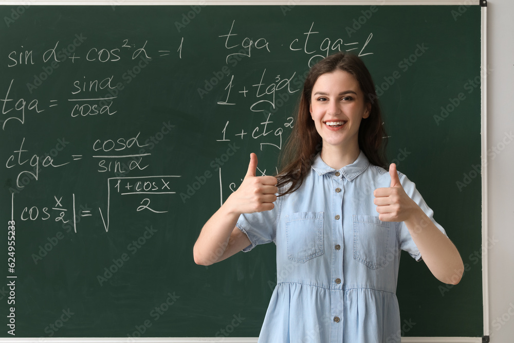 Female Math teacher showing thumbs-up near chalkboard in classroom