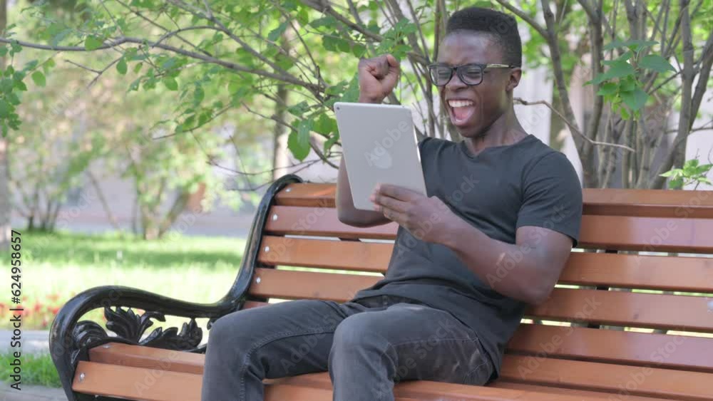 Young African Man Celebrating Success on Tablet while Sitting Outdoor on a Bench Young African Man Celebrating Success on Tablet while Sitting Outdoor on a Bench