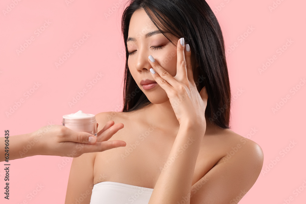 Beautiful Asian woman and hand with cream on pink background Beautiful Asian woman and hand with cream on pink background