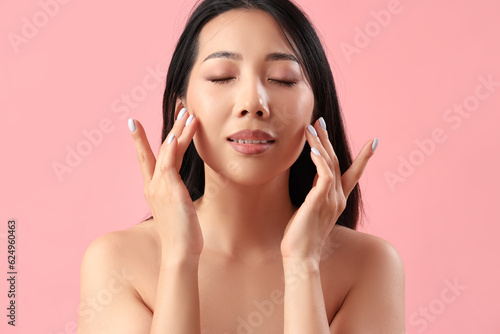Skincare routine and beauty wellness, young Asian woman touching her face with eyes closed on a pink background