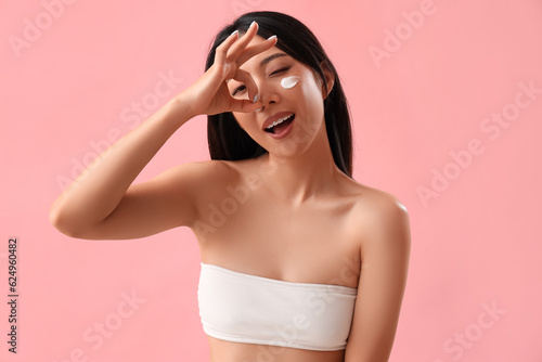 Beautiful Asian woman with cream on her face showing OK against pink background