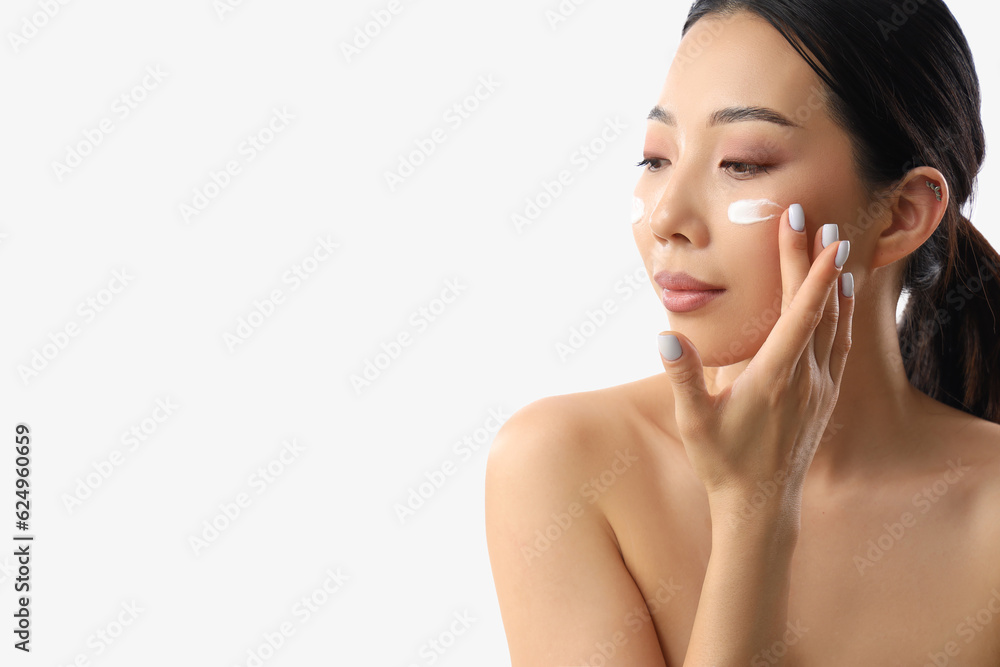 Beautiful Asian woman applying facial cream against white background