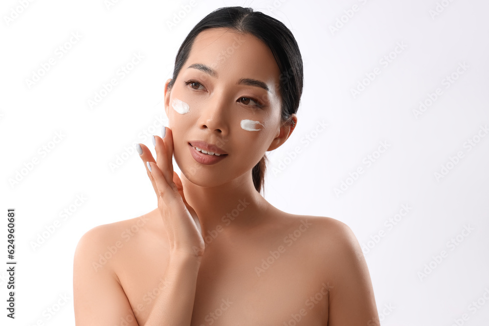 Beautiful Asian woman applying facial cream against white background Beautiful Asian woman applying facial cream against white background