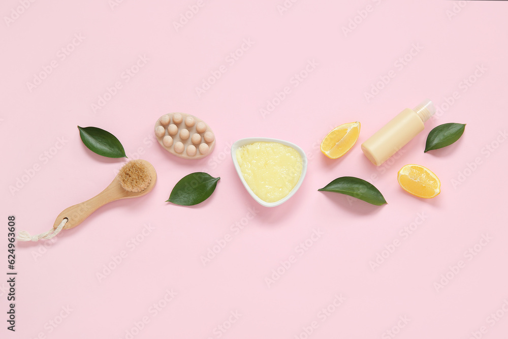 Bowl of lemon body scrub with cosmetic bottle, massage soap bar and brush on pink background