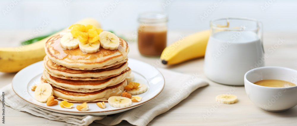 A stack of oatmeal banana pancakes with fresh banana slices, walnuts and honey on top and a cup of tea on a white wooden background. A healthy breakfast. Copy space - obrazy, fototapety, plakaty 