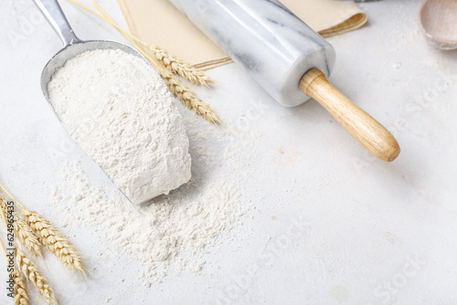 Scoop with wheat flour and rolling pin on white background