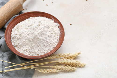 Bowl with wheat flour and spikelets on white table, closeup