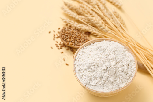 Bowl with wheat flour and spikelets on yellow background, closeup