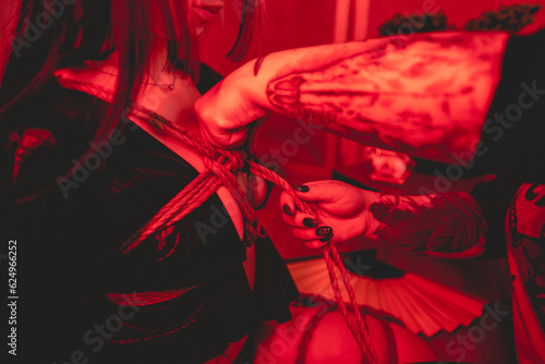 The beauty and elegance of the art of shibari bondage: woman rope tying and knots in a young and attractive woman with a little black kimono, in a beautiful red-lit traditional japanese room