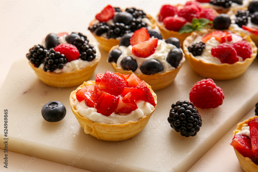 Board of tasty tartlets with whipped cream and berries on beige background Board of tasty tartlets with whipped cream and berries on beige background