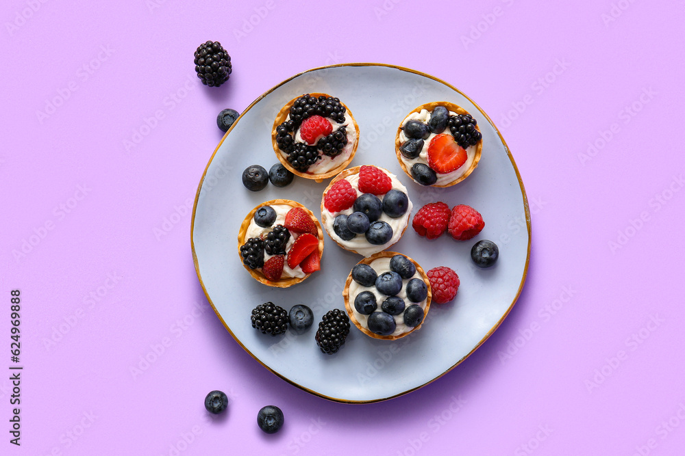 Plate of tasty tartlets with whipped cream and berries on lilac background Plate of tasty tartlets with whipped cream and berries on lilac background