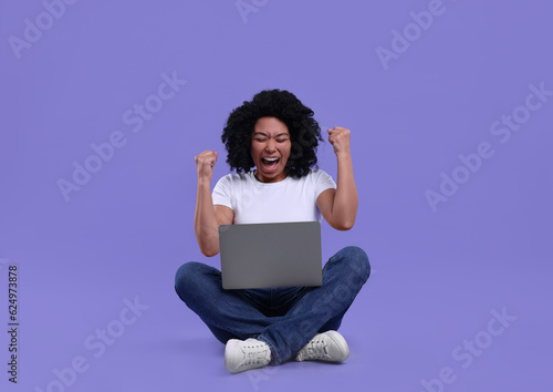 Emotional young woman using laptop on purple background © New Africa