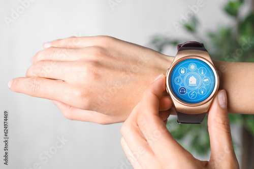 Woman setting smart home control system via smartwatch indoors, closeup. App interface with icons on display