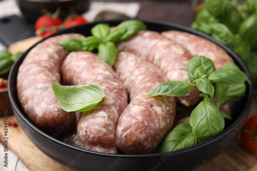 Raw homemade sausages and basil leaves on table, closeup
