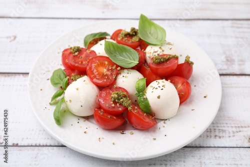 Tasty salad Caprese with tomatoes, mozzarella balls and basil on white wooden table, closeup