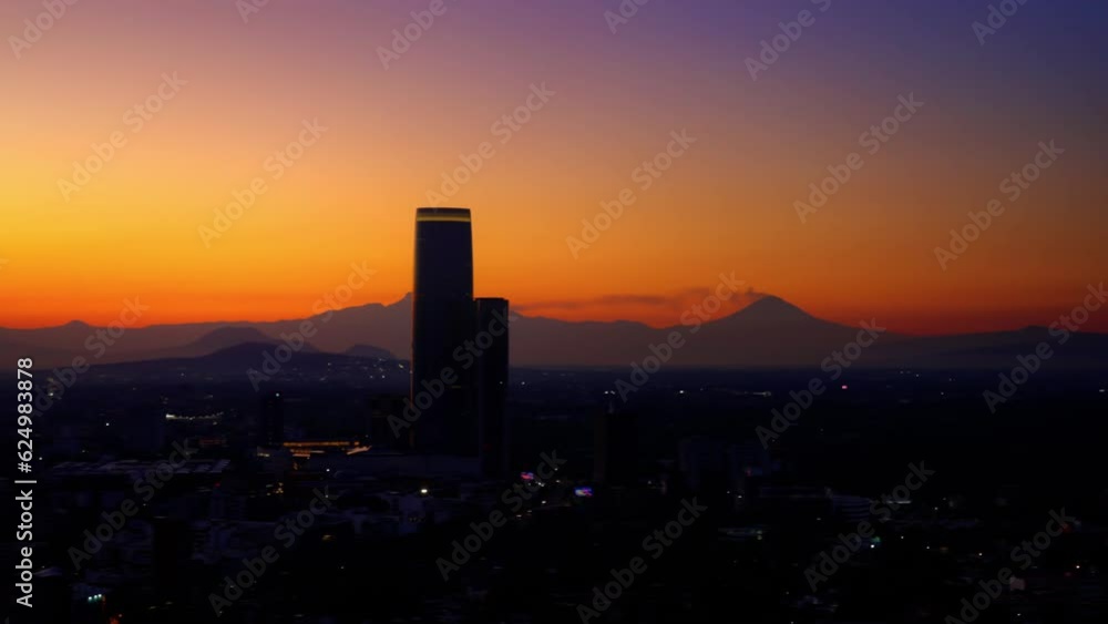 Aerial view of amazing sunrise over modern city with skyscraper of Mexico City with tall Mitikah Tower at bright orange sunrise with blue sky over foggy mountains in morning time