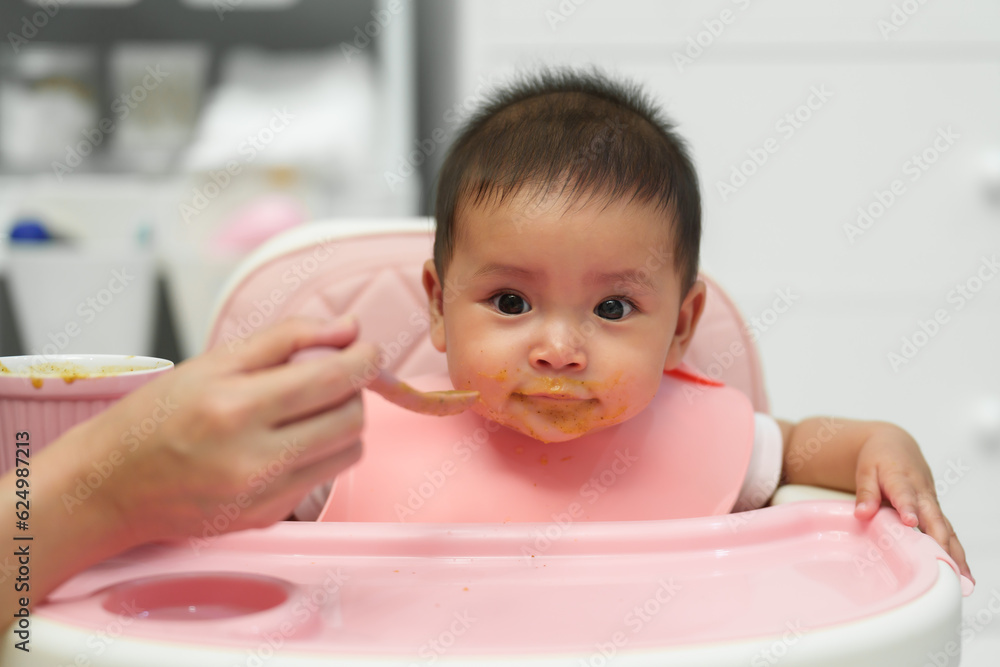 mother feeding food to her infant baby eating with spoon at home mother feeding food to her infant baby eating with spoon at home