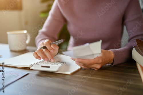 Fotografie A woman sitting at a table using a calculator, and planning her household expenses